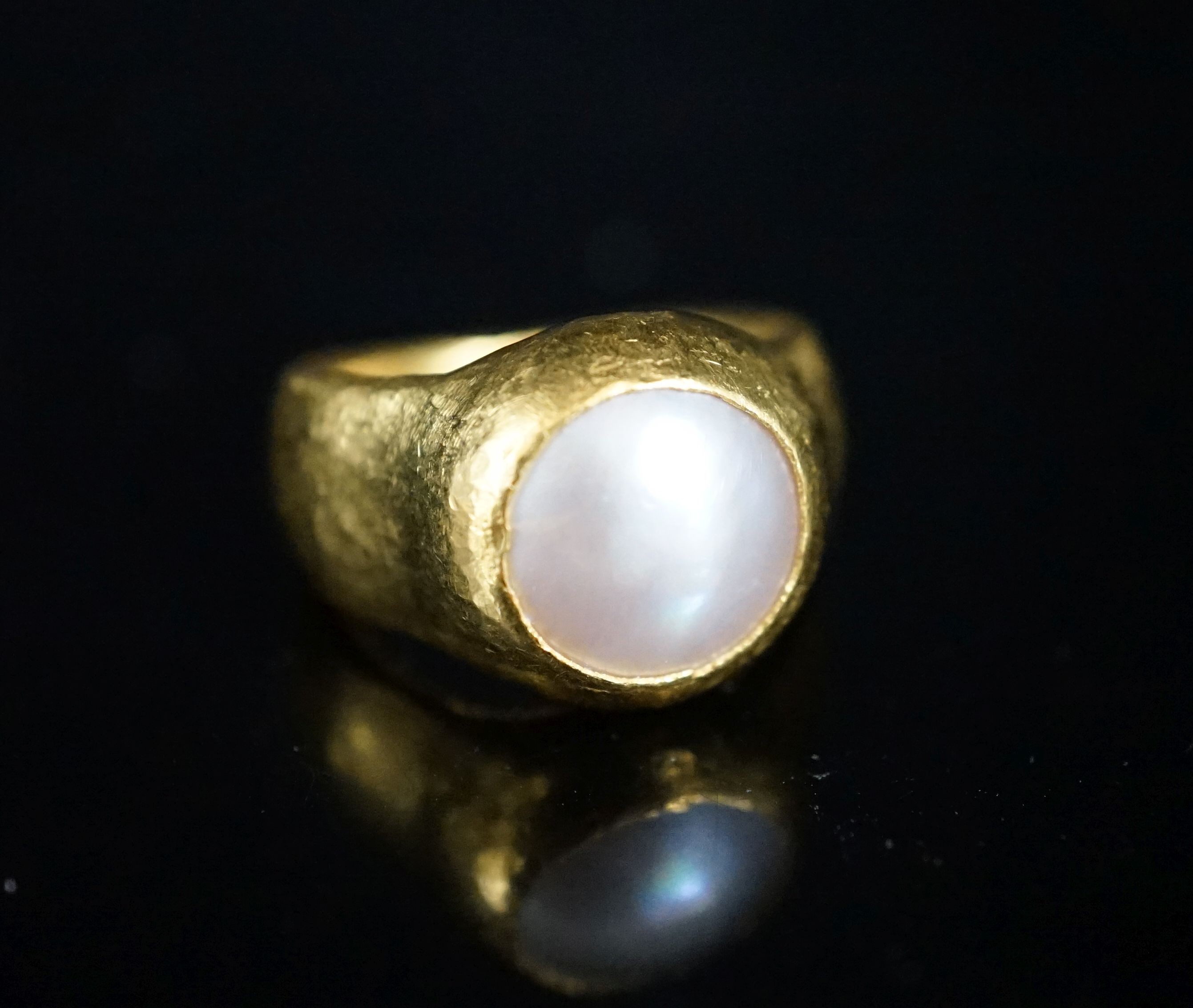 A planished yellow metal (inscribed 24k) and mother of pearl mounted ring, indistinctly signed, size N, gross 11.6 grams.